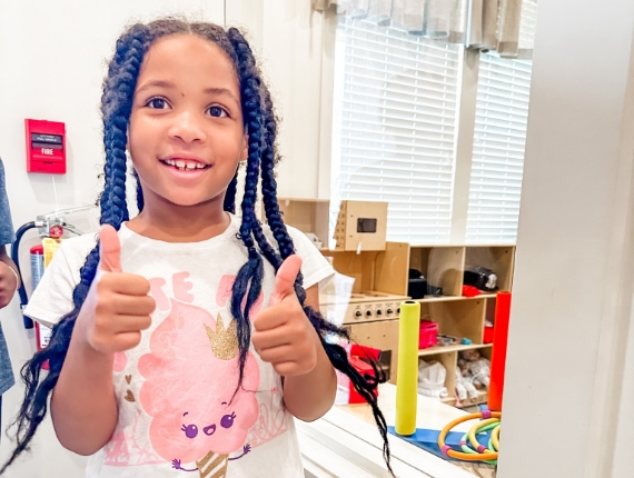 a little girl poses for the camera with her thumbs up